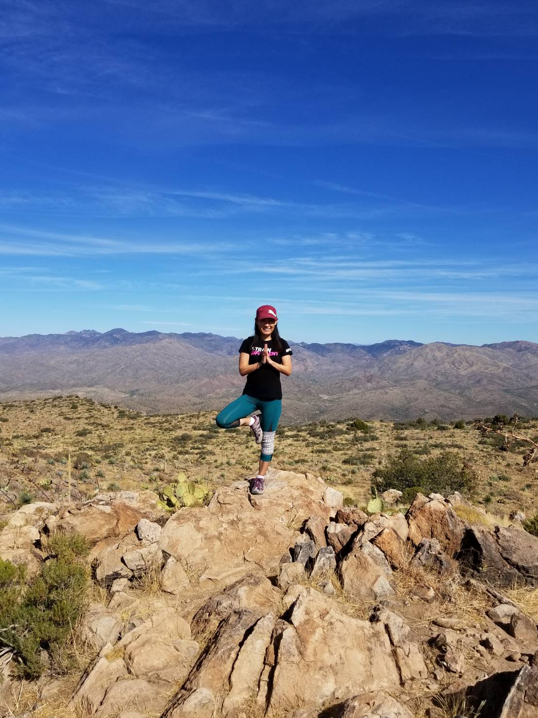 Yumi Urata in tree pose on a rock overlooking a desert mountain landscape